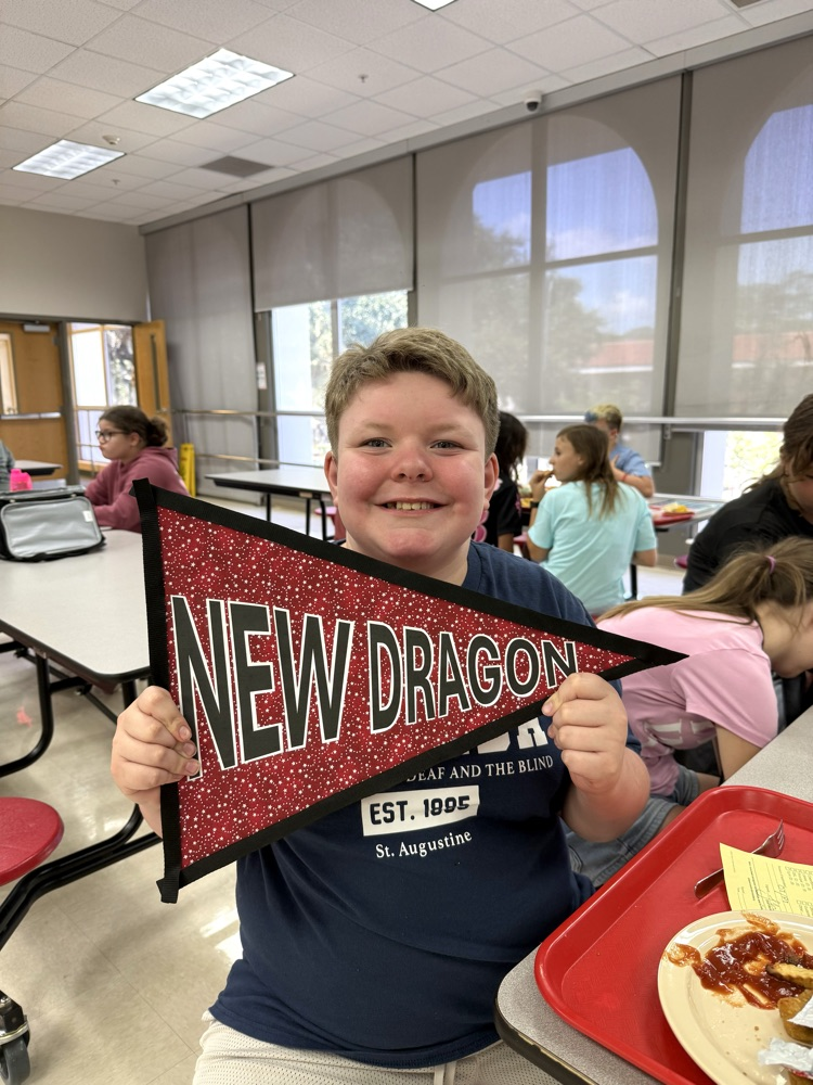 A DMS boy is holding a sign that says, “New Dragon”, and smiling.