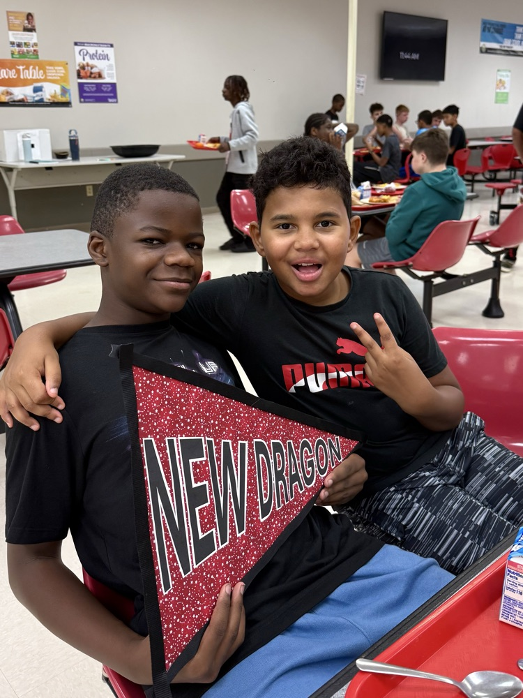 Two DMS boys are holding a sign that says, “New Dragon”, and smiling.