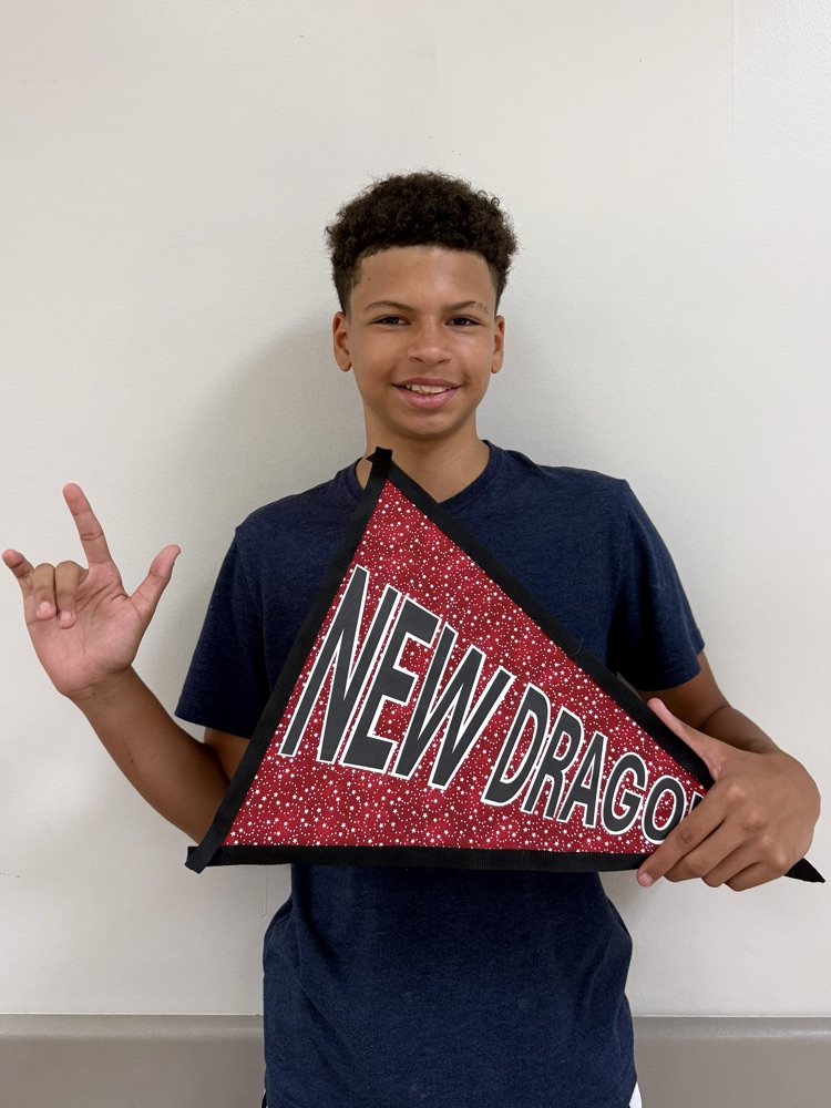 A DMS boy is holding a sign that says, “New Dragon”, and smiling.