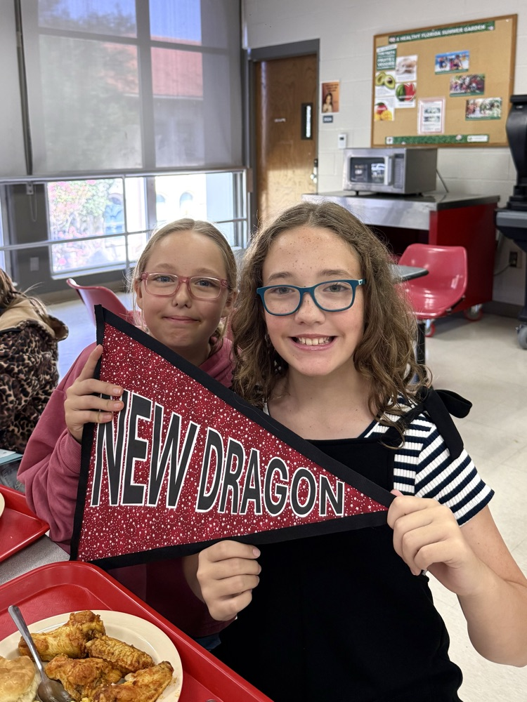 Two DMS girls are holding a sign that says, “New Dragon”, and smiling.