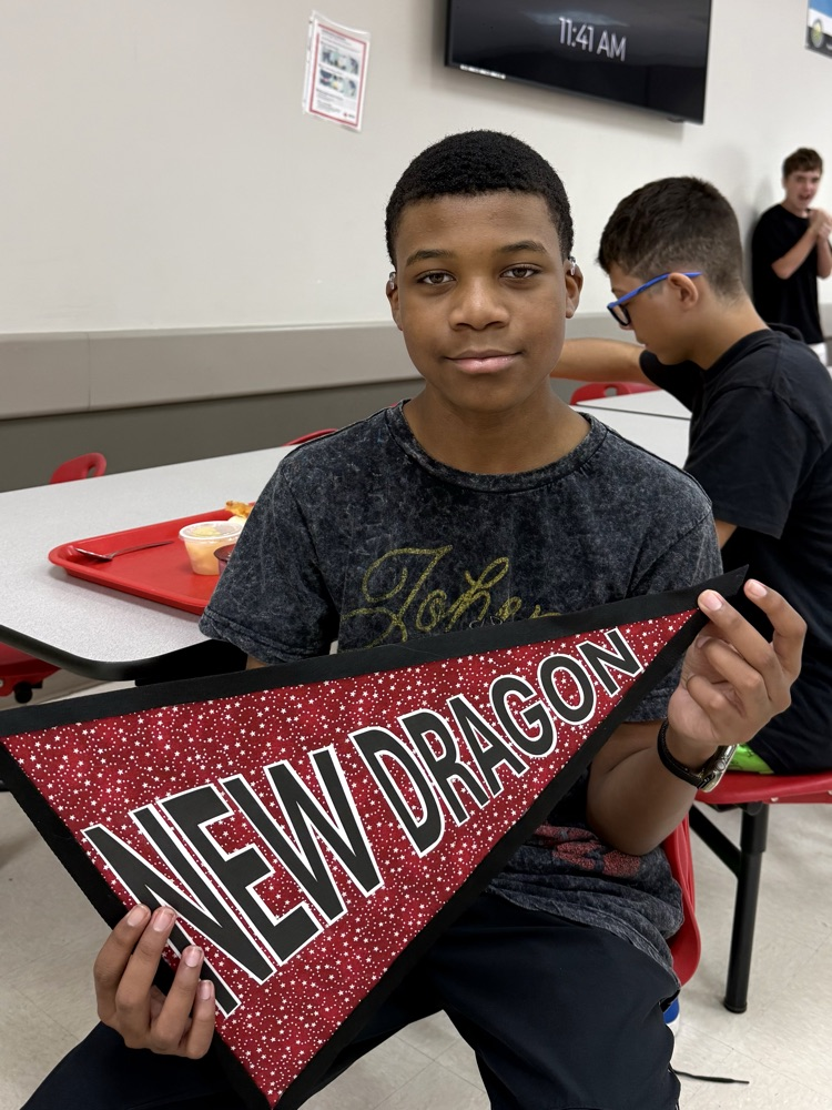 A DMS boy is holding a sign that says, “New Dragon”, and smiling.