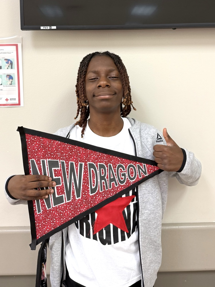 A DMS boy is holding a sign that says, “New Dragon”, and smiling.