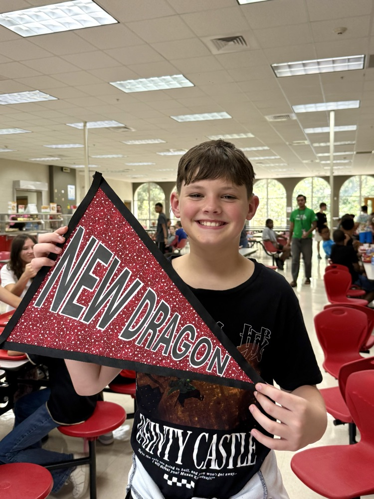 A DMS boy is holding a sign that says, “New Dragon”, and smiling.