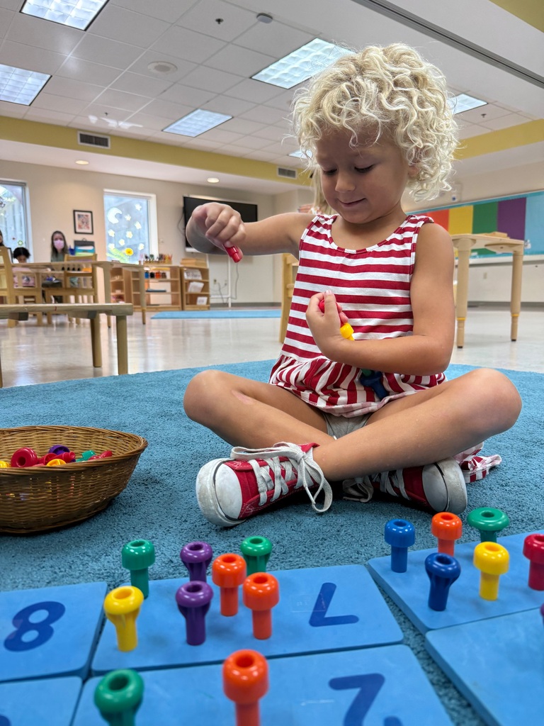 Student sits on blue carpet and plays with toys. 