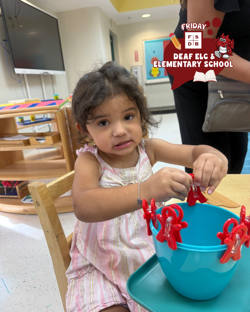 Student sits in her chair smiles while holding red clips in a blue bowl. 