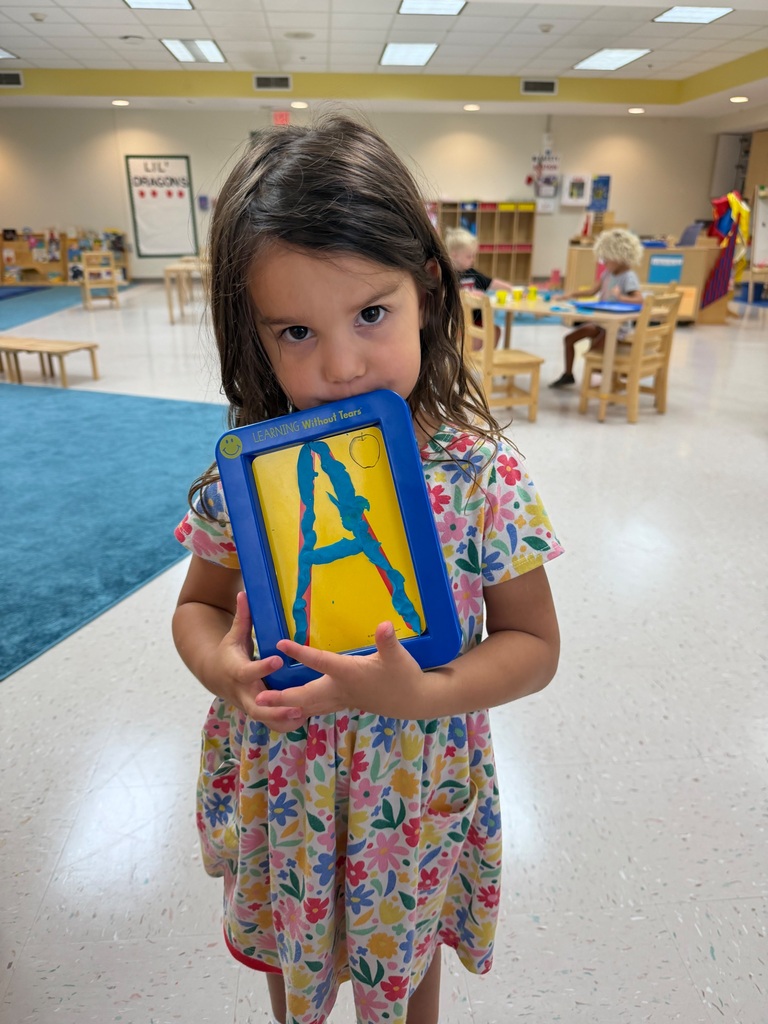 Student holds her work that has letter A smiles for photo.