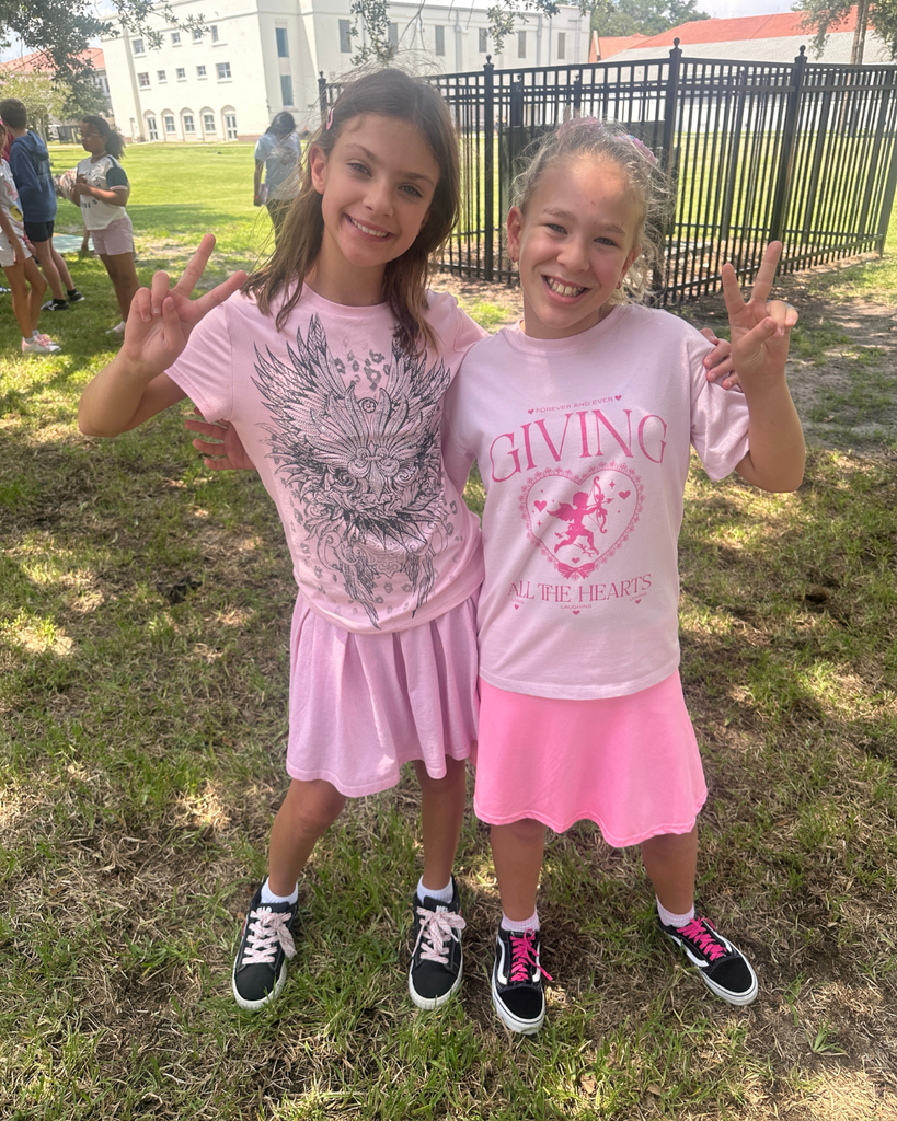 Two students wear all pink hold peace signs for a photo together outside.