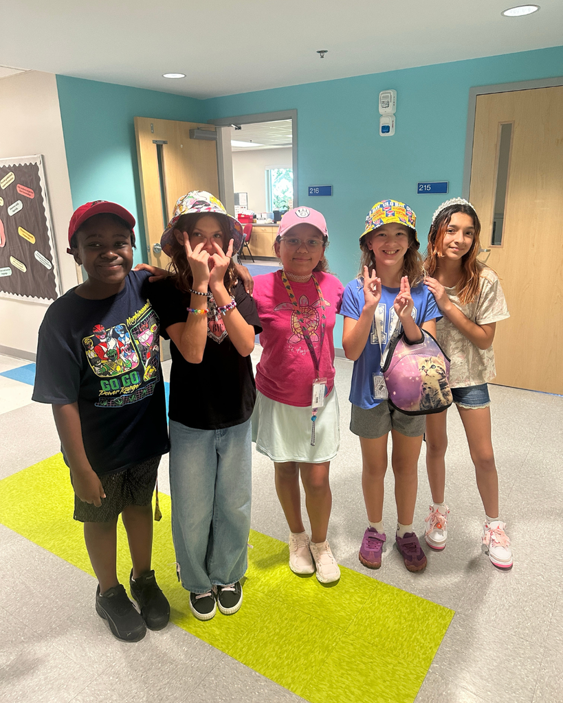A group of students wear hats smiling for a photo inside the hallway.
