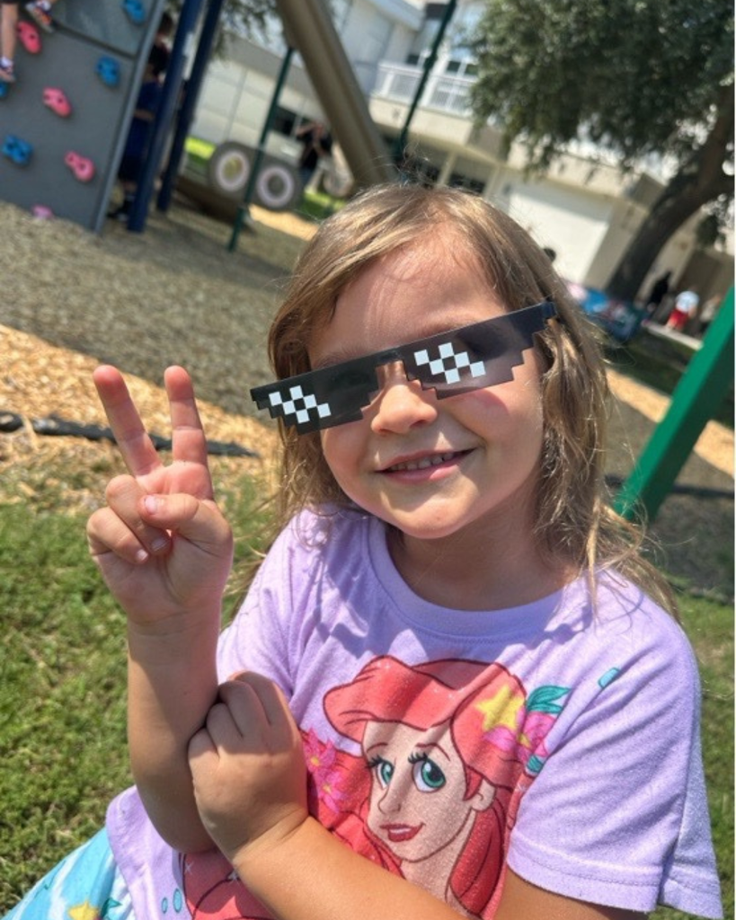 A student wearing fake sunglasses peace sign and smiles for the photo.