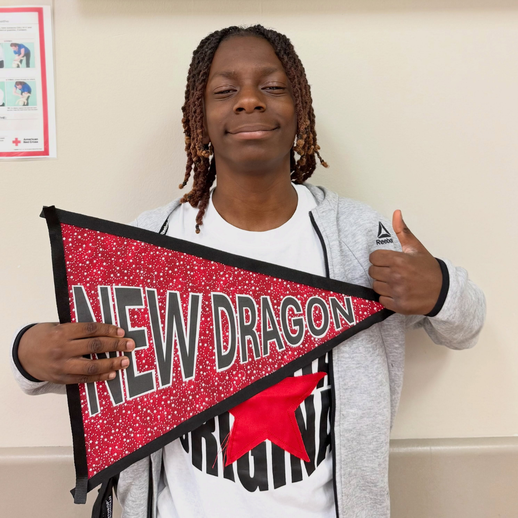 A student holds the "New Dragon" flag and gives a thumbs up. 