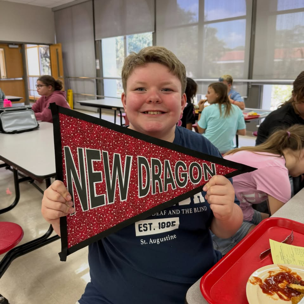 A student smiles and holds the "New Dragon" flag. 
