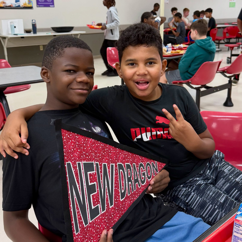 Two students smile together holding the "New Dragon" sign. 