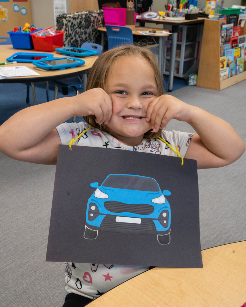 A student smiles with a blue car necklace inside the classroom.
