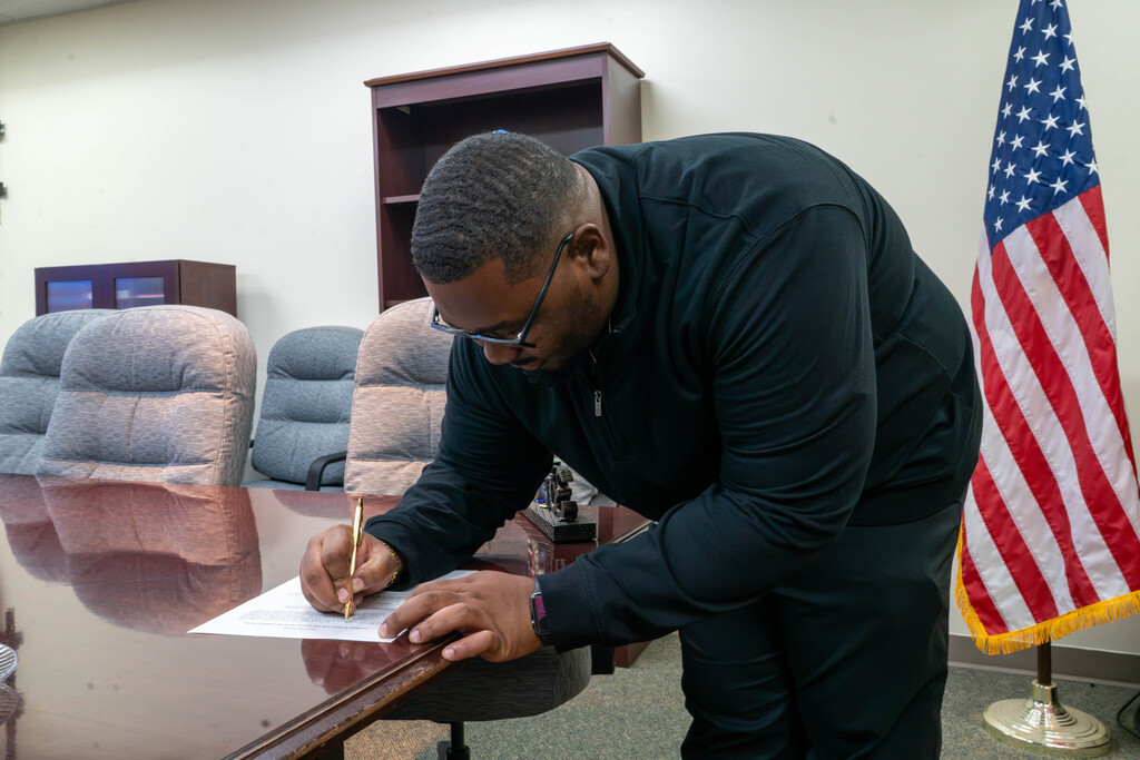 Ne'Darrius signs a paper at a desk inside campus police building.