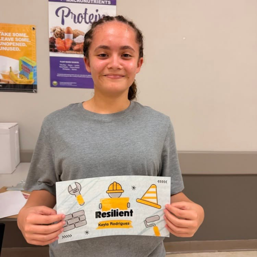 A student smiles with her 'Resilient" card inside the classroom. 
