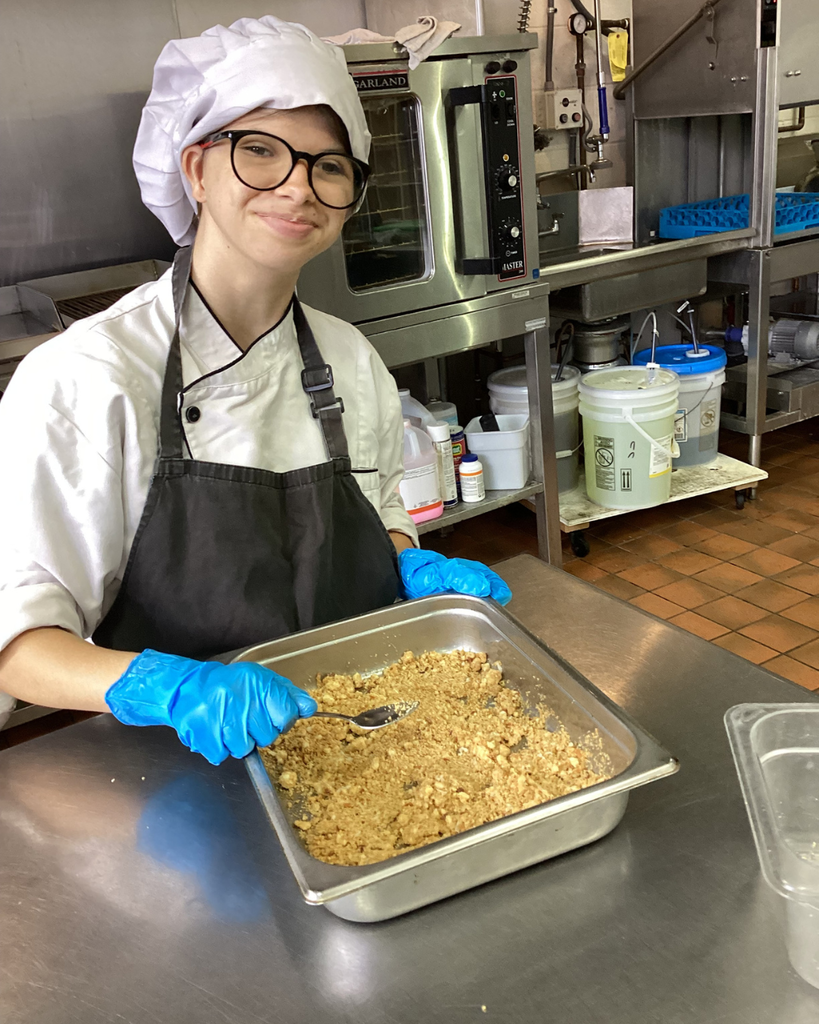 A student smiles as she prepares the dish inside the kitchen.