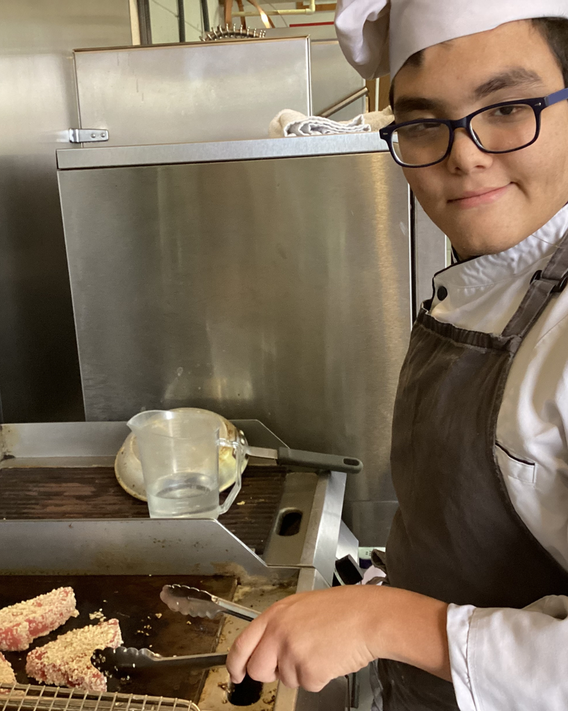 A close up of a student cooking tuna on the stove inside the kitchen.