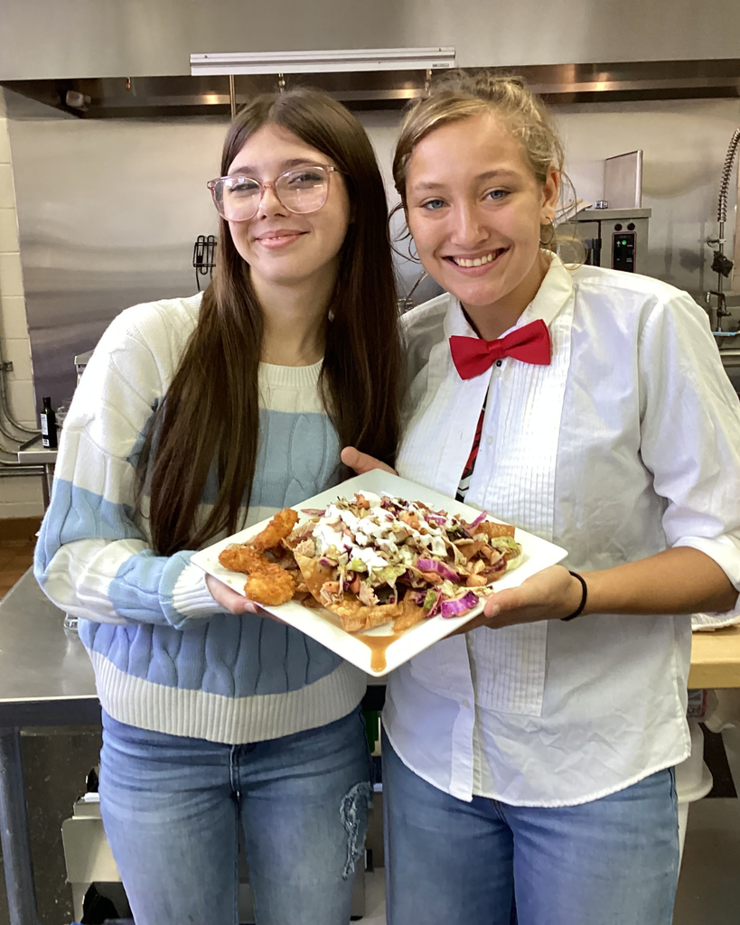 Two students smile with the finalized plate inside the kitchen.