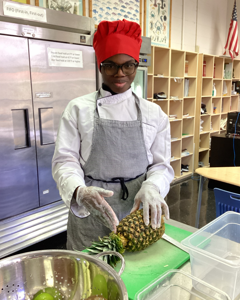 A student smiles with a pineapple inside the kitchen. .