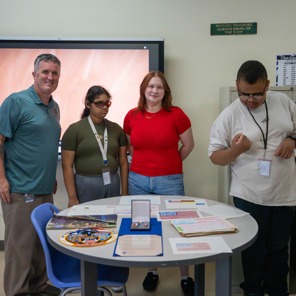 Group of students smile with Mr. Ward inside his classroom. 
