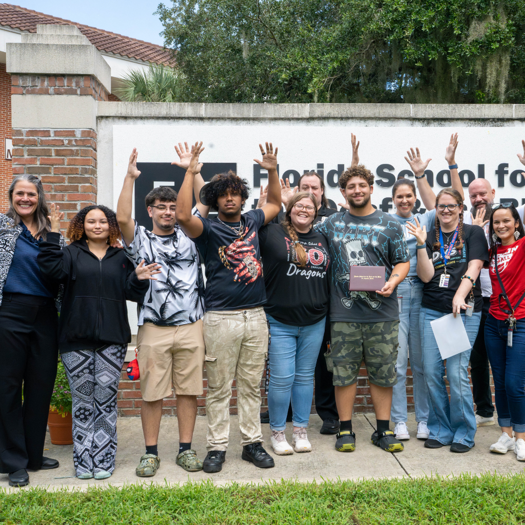 Group of staff and friends wave their hands in the air with LaSean in the middle. 