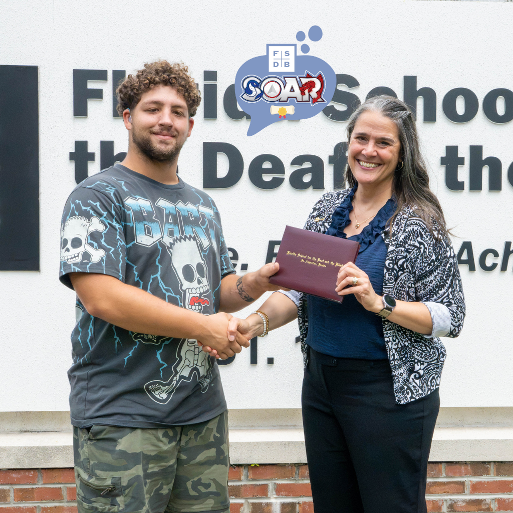 President Snow and LaSean hold the diploma and shake hands in front of the FSDB sign. 