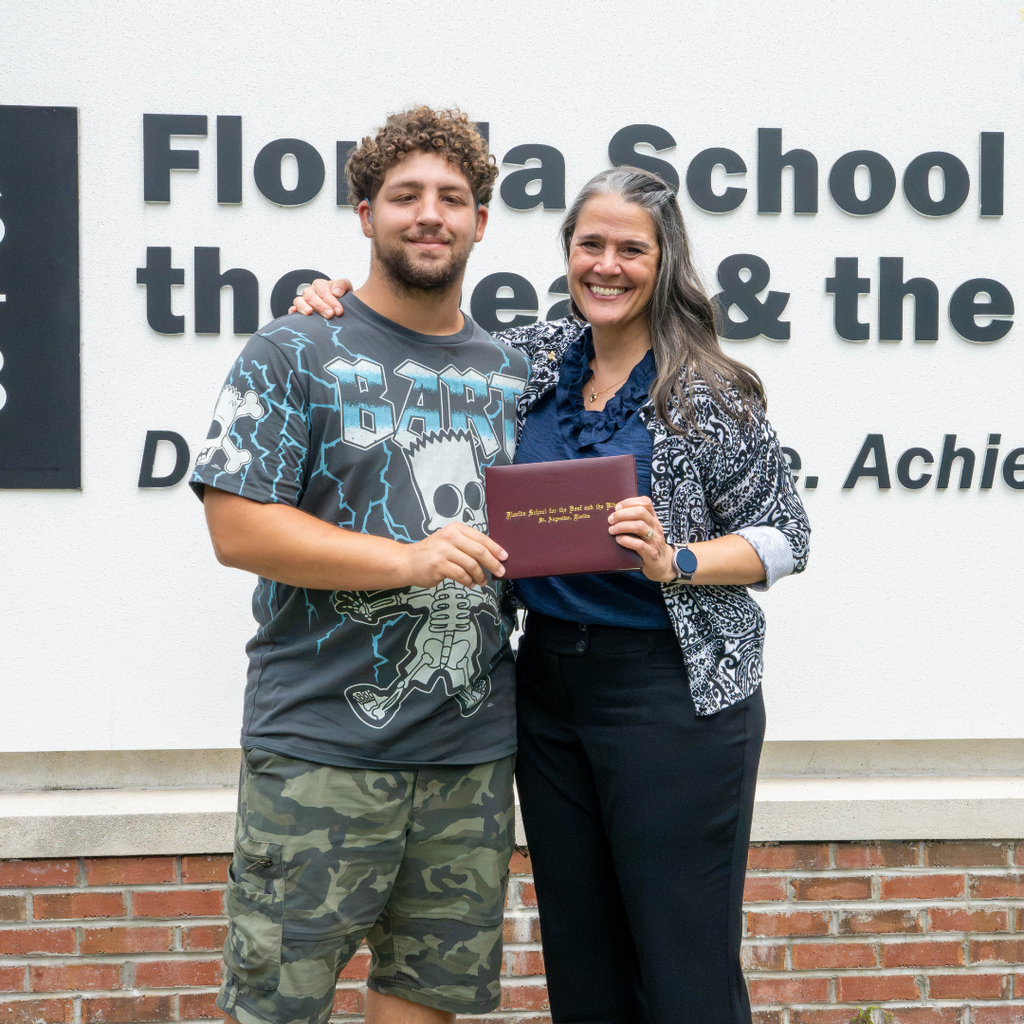 President Snow and LaSean hold the diploma and hug for a photo with the FSDB sign in the background. 