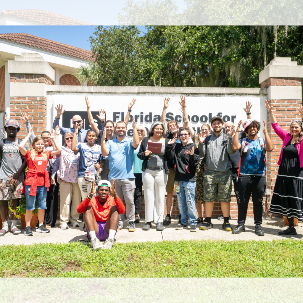 Group of staff and students wave their hands in the air with Jaylene in the middle by the FSDB sign. 