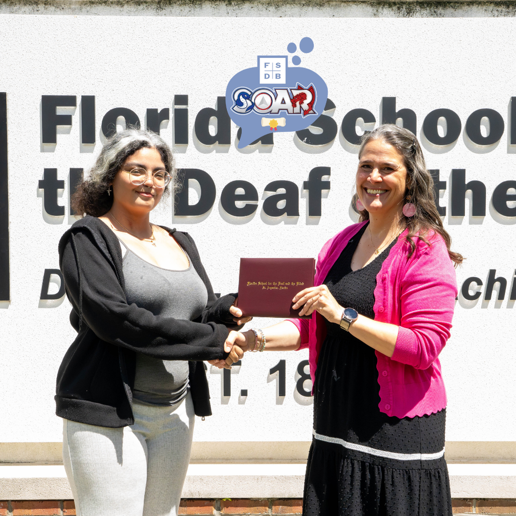 President Snow and Jaylene hold the diploma and shake hands by the FSDB sign. 