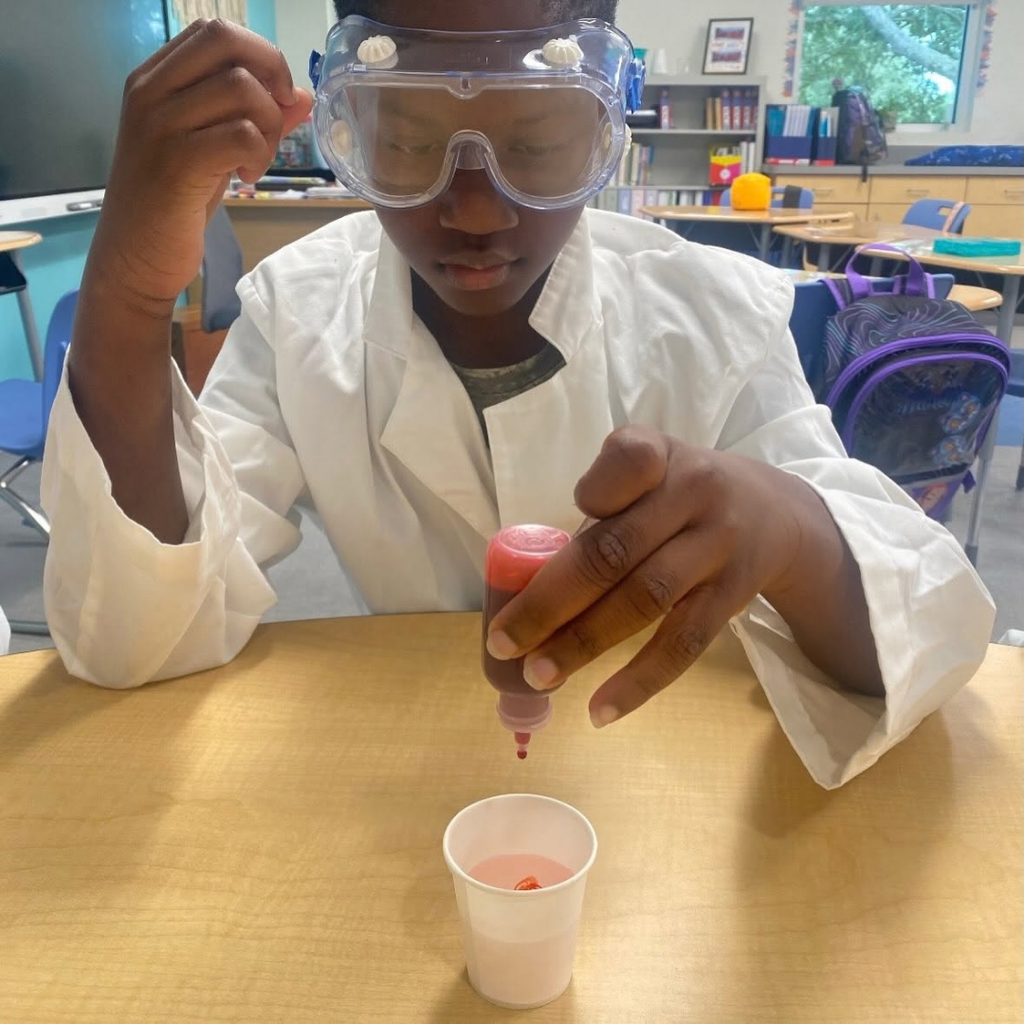 A close up photo of a student dropping red drops in a cup.