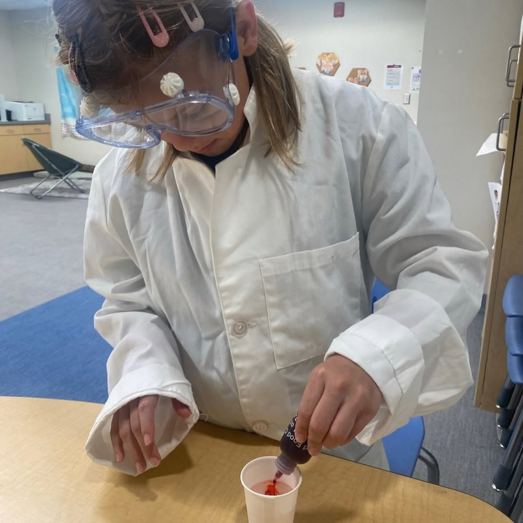 A close up photo of a student dropping red drops into cup.