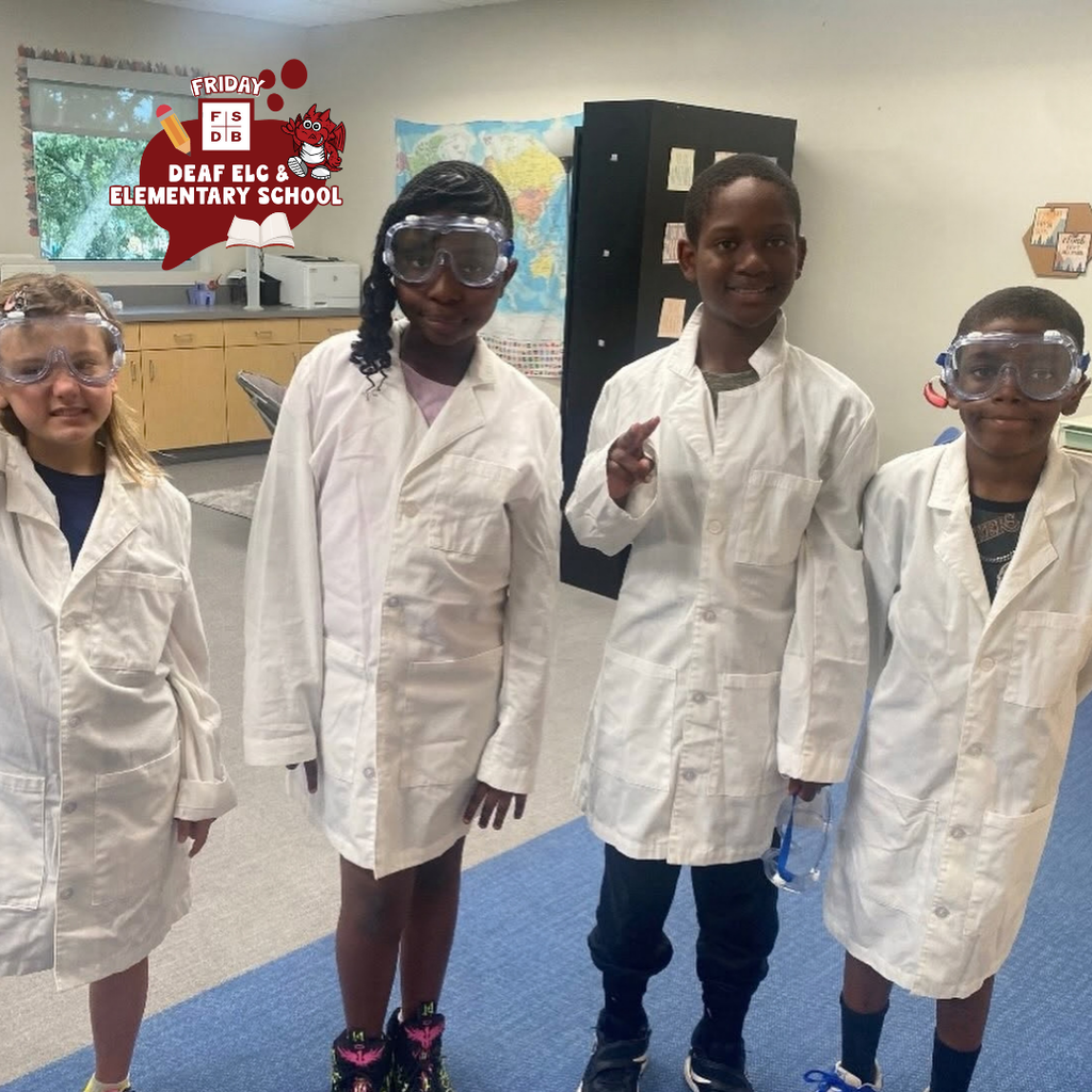 Four students dressed in white science jackets and googles inside the classroom.