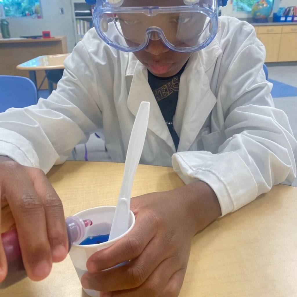 A close up photo of a student dropping red drops into the blue water.