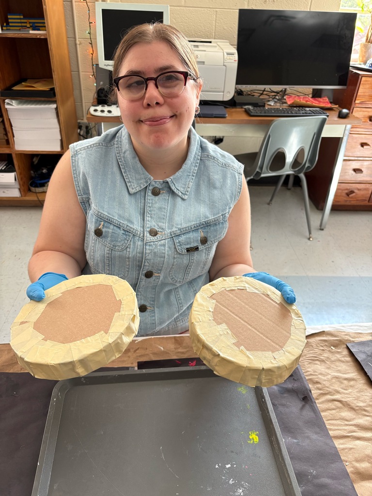 Paige smiles as she holds up two layers of the paper mache cake she is constructing.