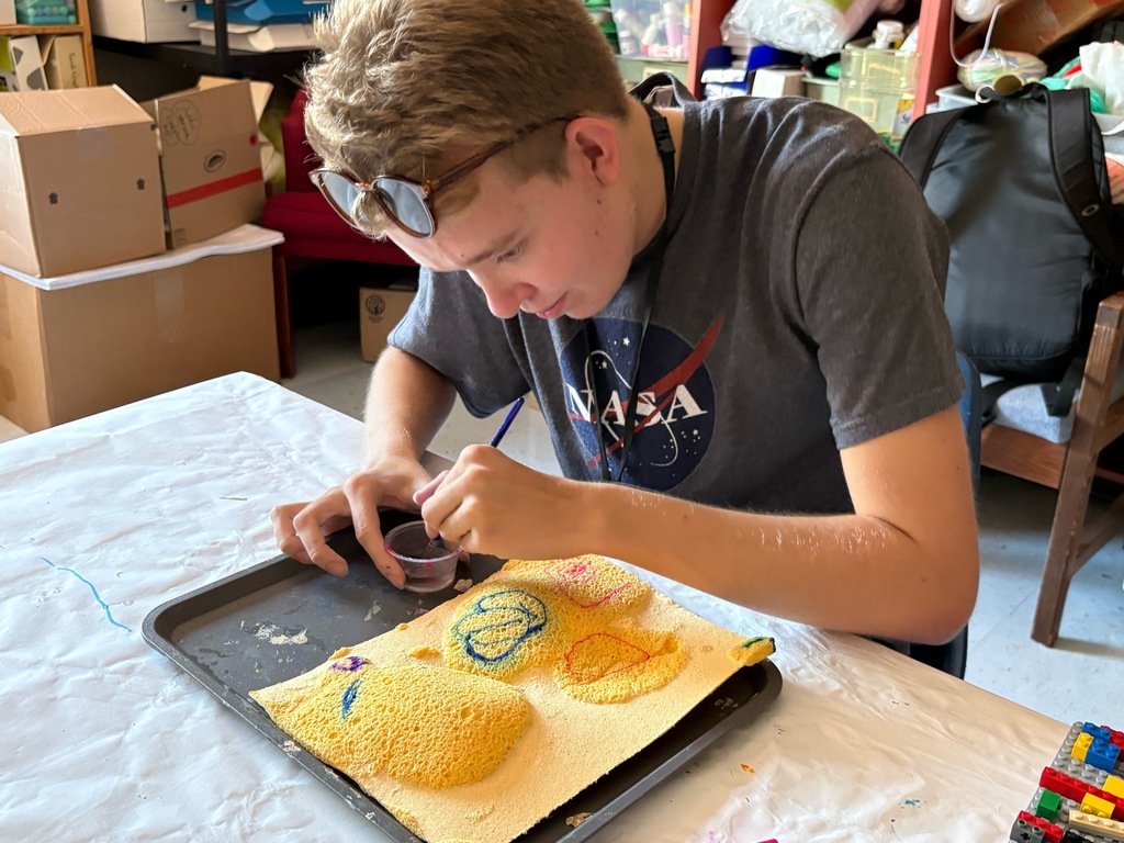 Erik uses a paintbrush to apply water to swell paper to create a textured design.
