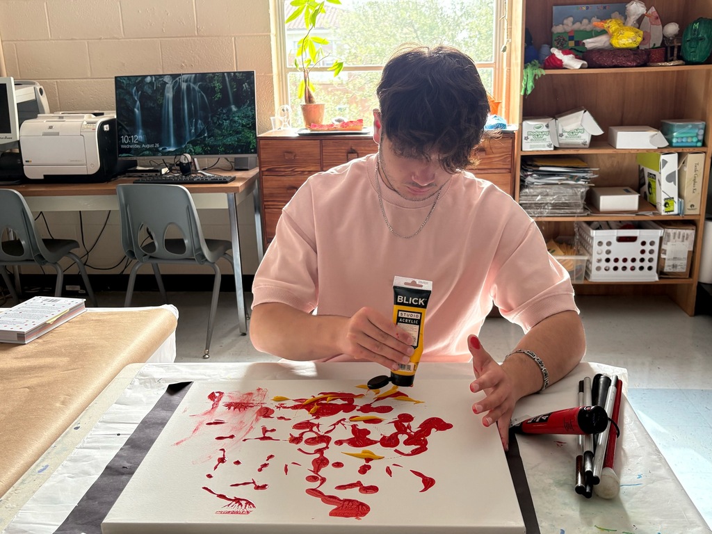 Aref squeezes thick yellow paint onto a canvas to create a textured background for his artwork.