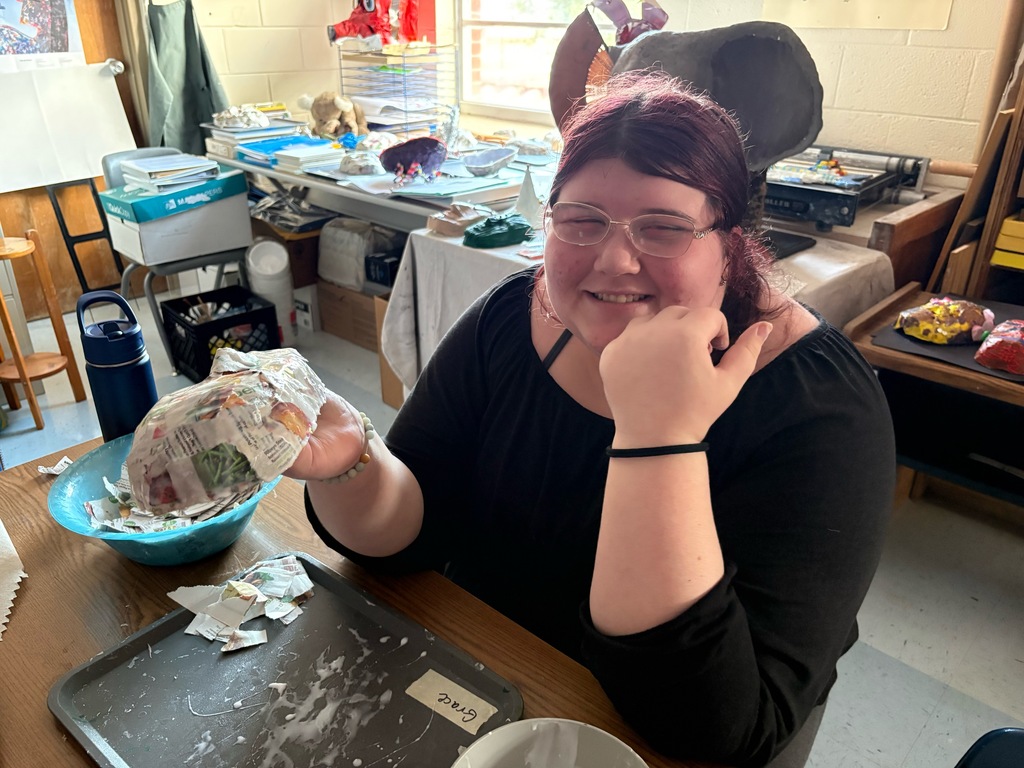 Grace is smiling and holding her paper mache mask.