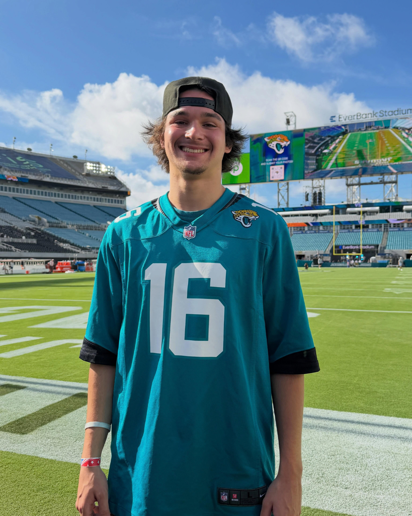 A photo of a deaf high school student wearing a Jag jersey smile for his photo on the field.