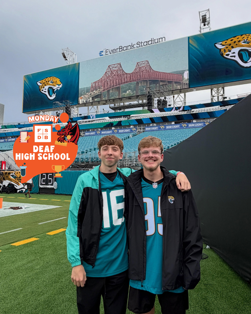 Two deaf high school students smile together wearing Jags jersey on the field of the Jags.