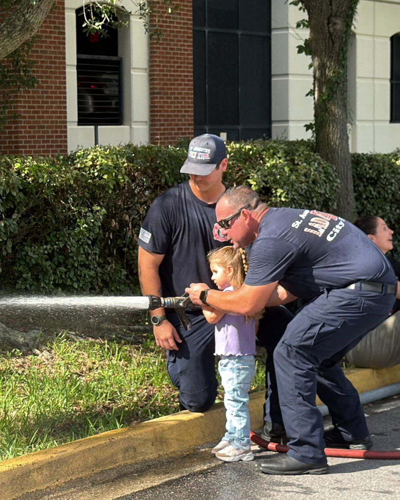 A ELC student is spraying the hose with two firefighters.