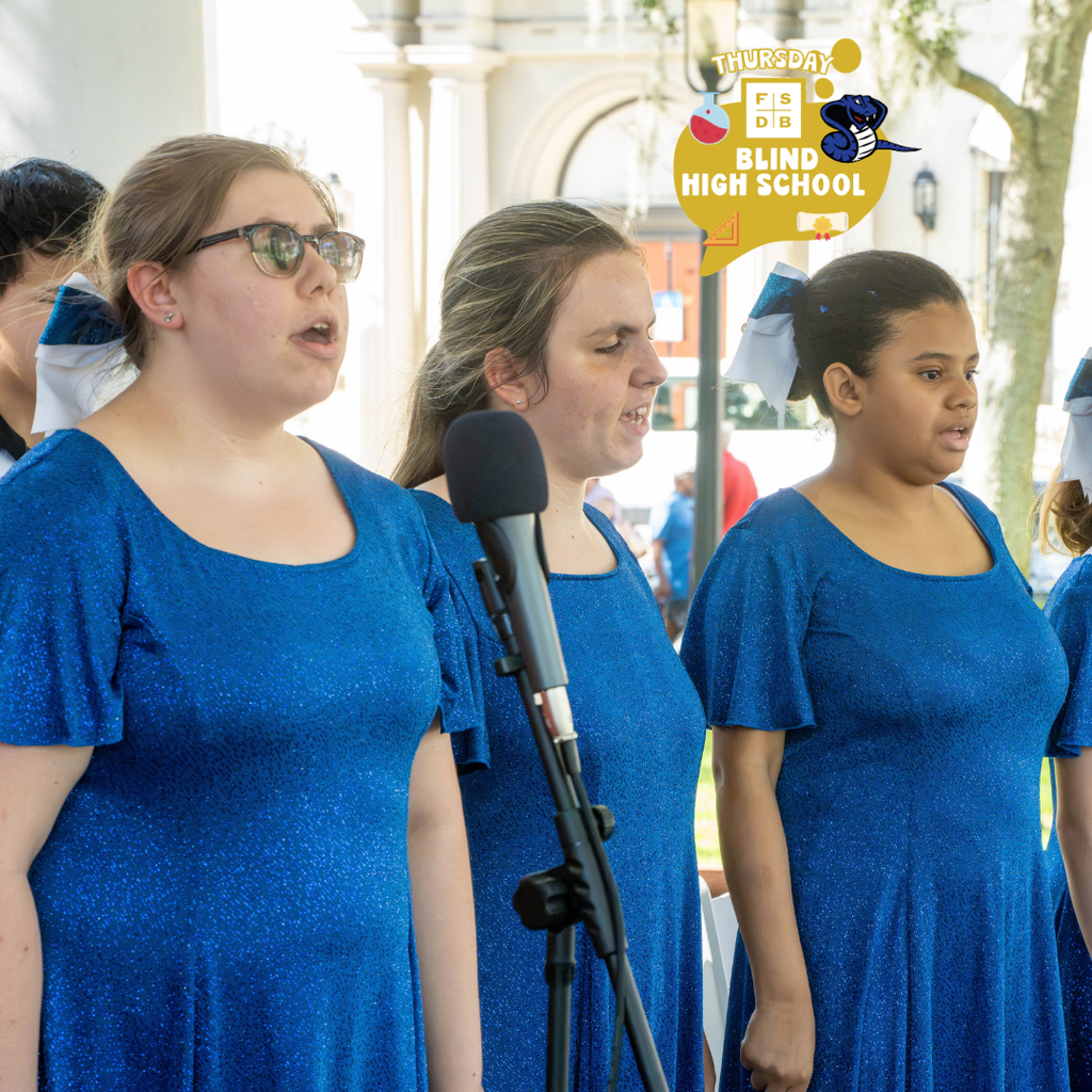 Three students wear blue sparkly dresses stand and sing outside downtown St. Augustine.