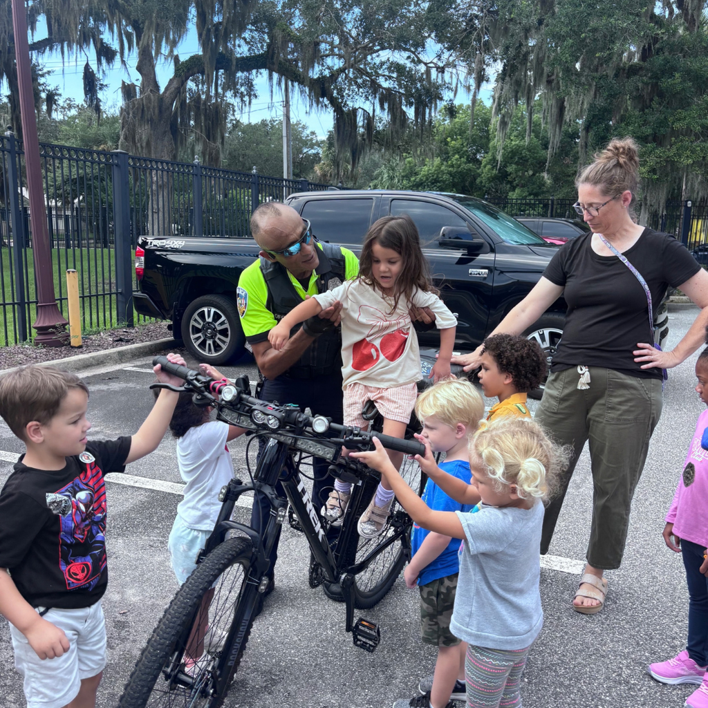 Campus police officer help a student go on his bike with other ELC students surrounding her.