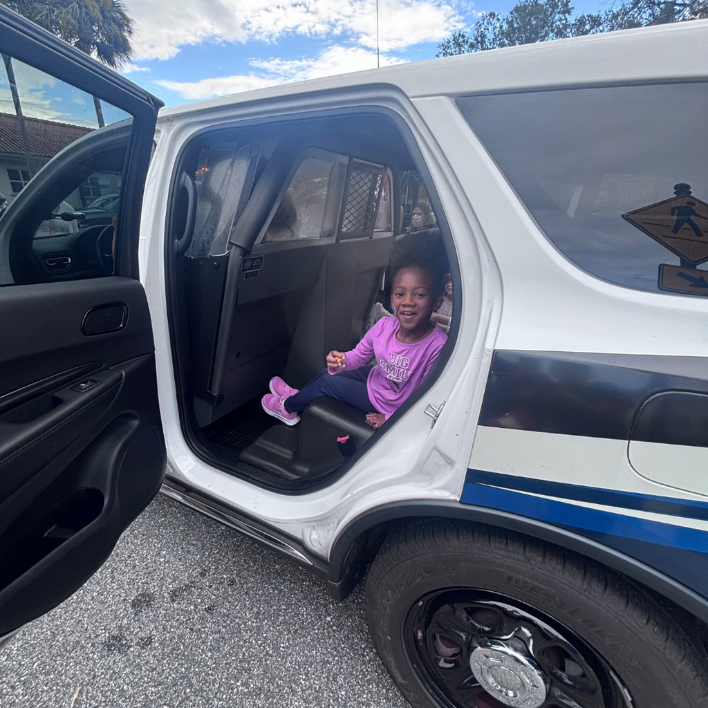 A student smiles as she sits in the back of a cop car. 