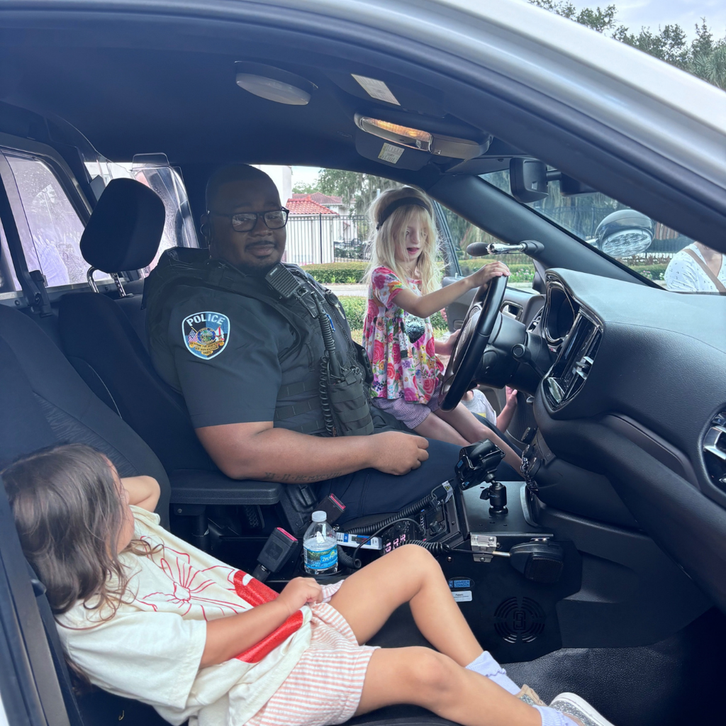 Two ELC students sit in the cop car with a campus police officer. 