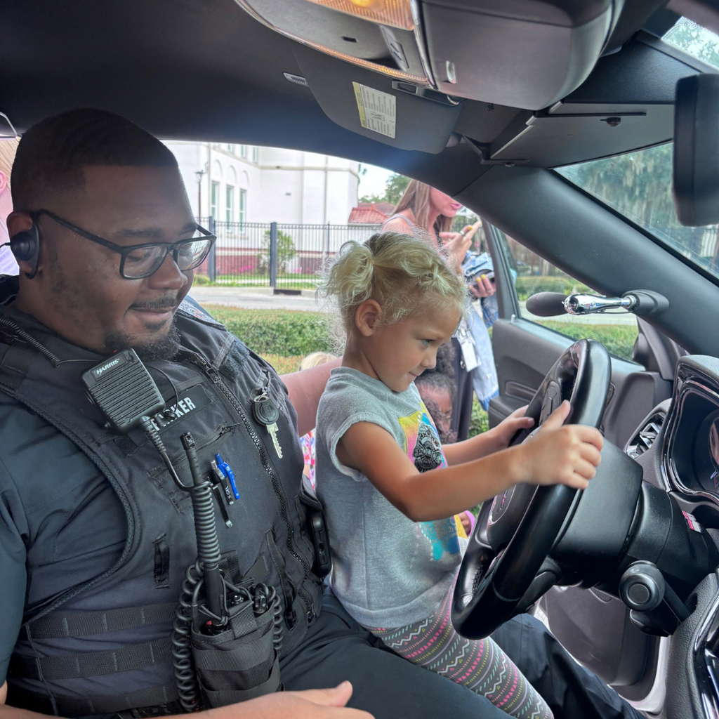 A student sit inside the cop car with a campus police officer. 