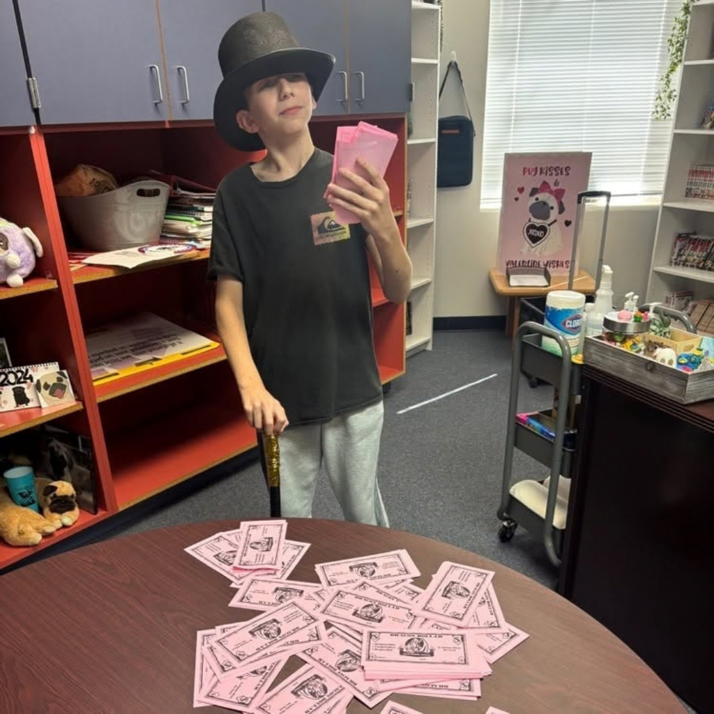 Student wears a black hat and looks at the pink money on the table.