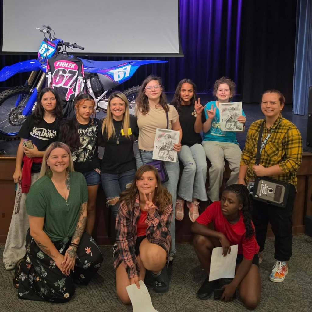 Group of DMS girls smile with Ashley on stage in Kirk.