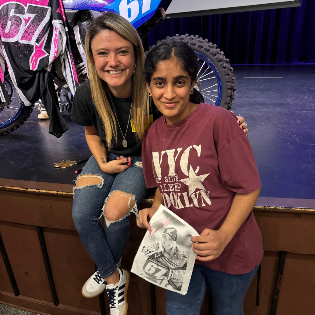 Ashley smiles on stage with a student holding her signature photo by Ashley.