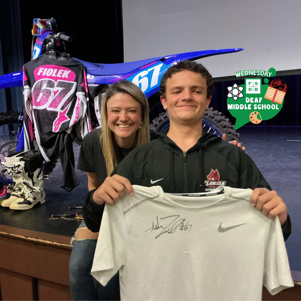 A student holds a shirt with ashleys signature smiles with her on stage in Kirk.