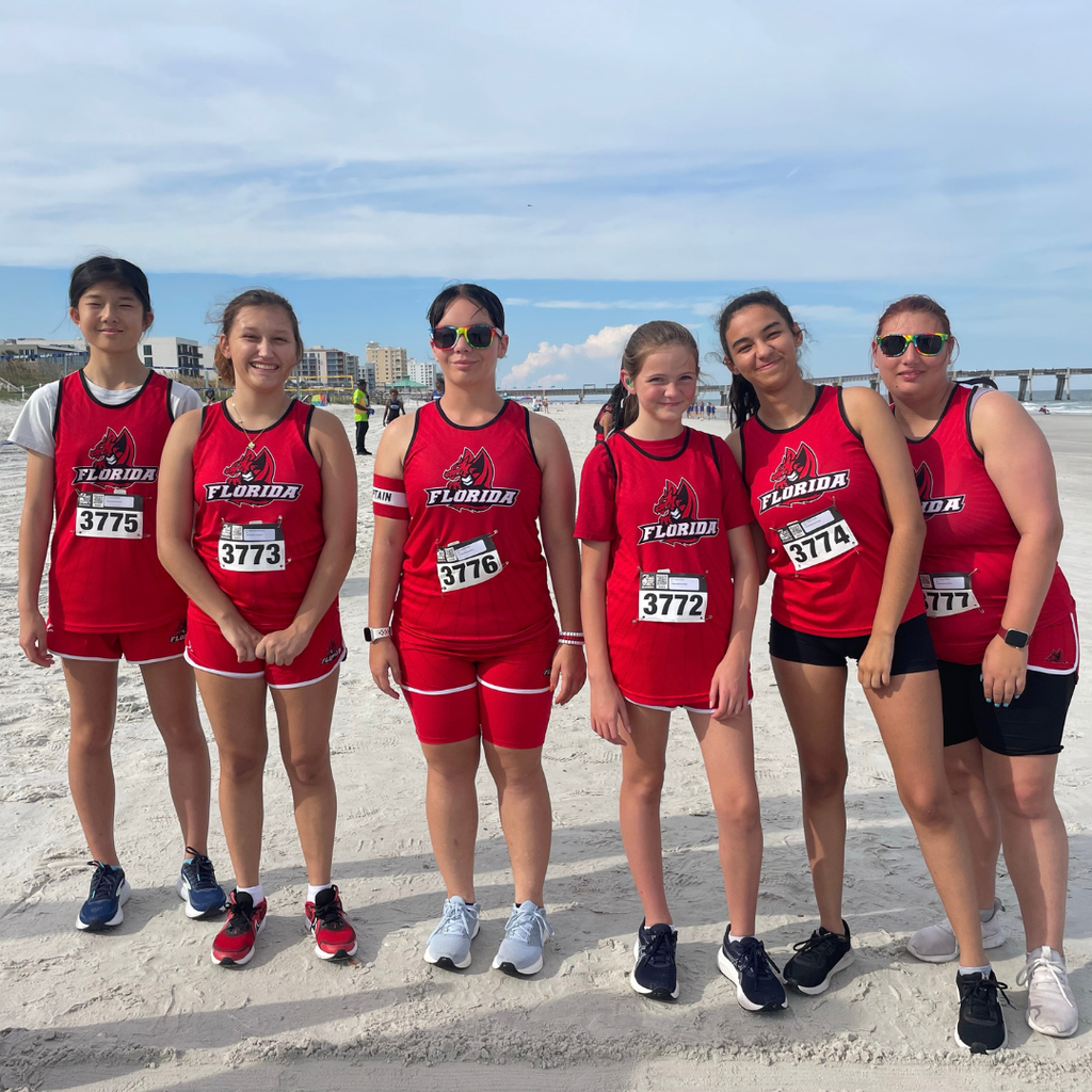 Girls Cross Country smile together as a team outside at the beach.
